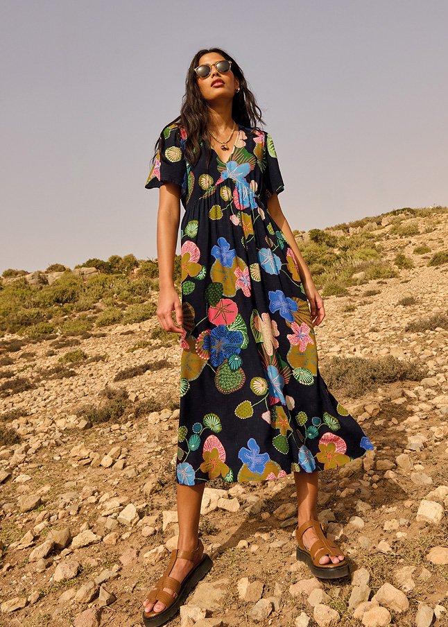 a woman in a floral dress standing on a rocky hill