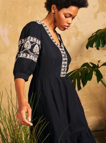 a woman in a black dress standing next to a plant