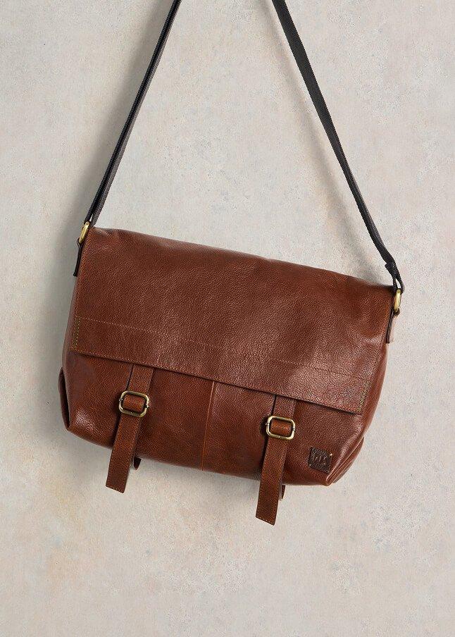 a brown leather cross body bag hanging from a wall