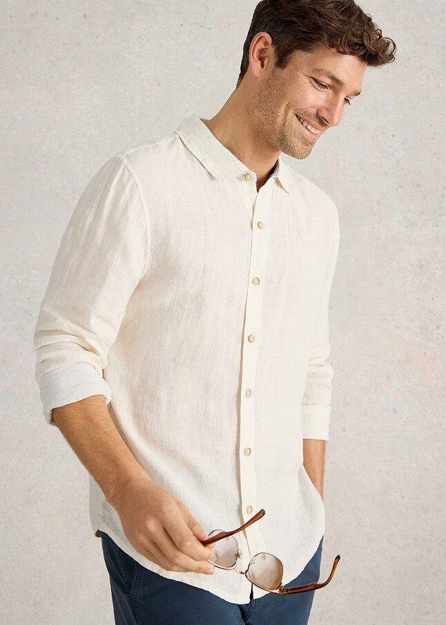 a man leaning against a wall with his hands in his pockets