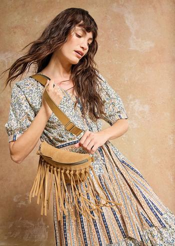 a woman in a dress and fringed bag is posing