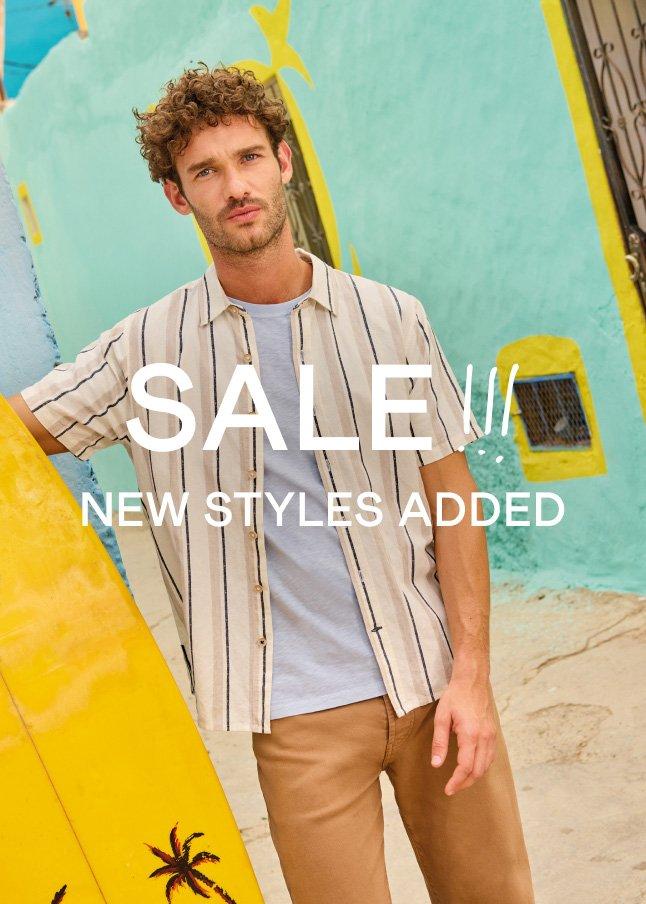 a man holding a surfboard with a sale sign in front of him