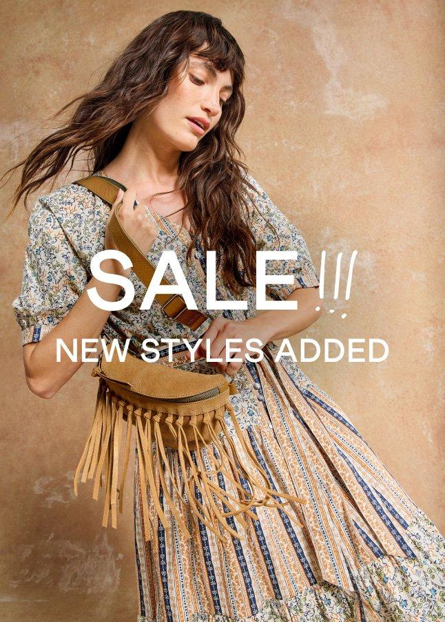 a woman in a dress with a fringe bag is holding a sign that says sale